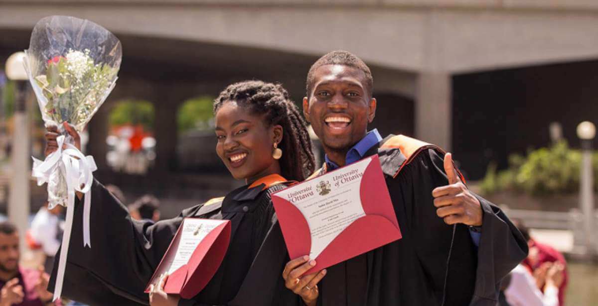 UOttawa graduates, smiling and holding their diplomas