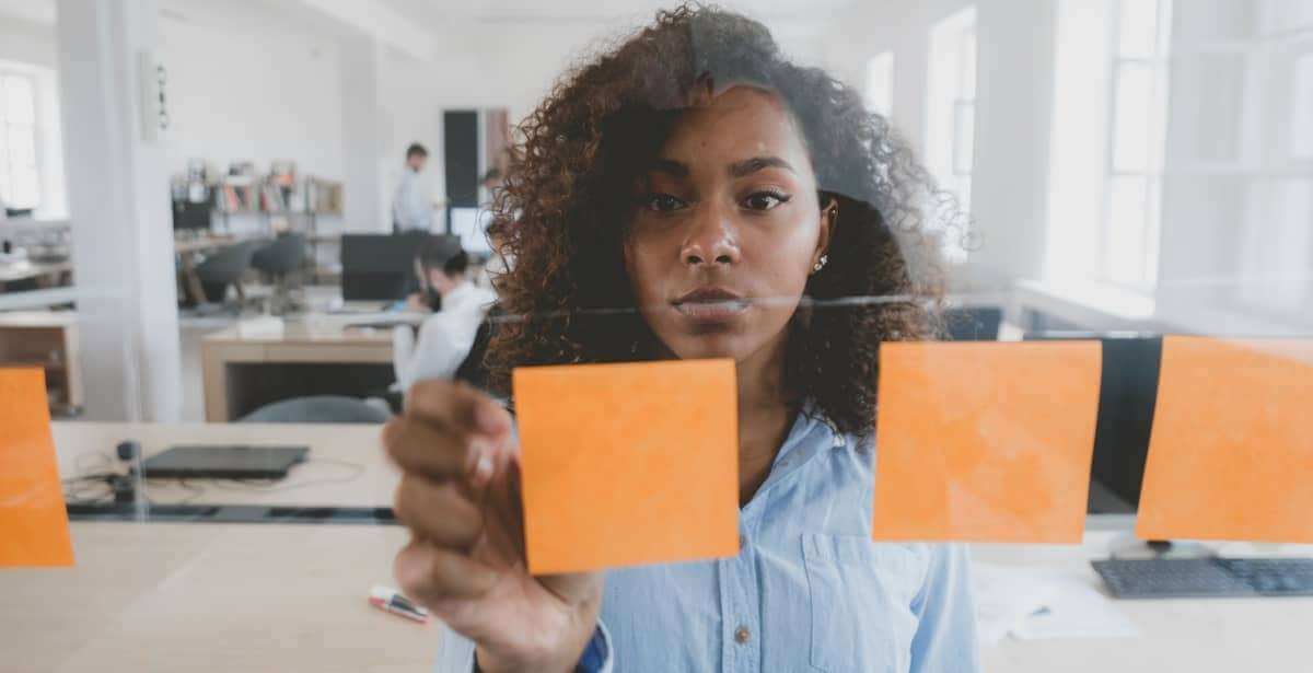 African American female employee looking onto a glass wall with sticky notes